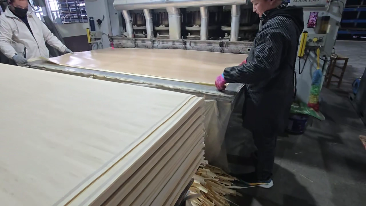 工人在熱壓機旁將飾面紙鋪放並對齊在板材上